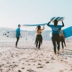 Group of surfers with blue surfboards heading to the ocean on a sunny beach.
